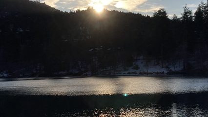Sunset over a lake with a forest in the background and clouds in the sky in the shape of angel wings.