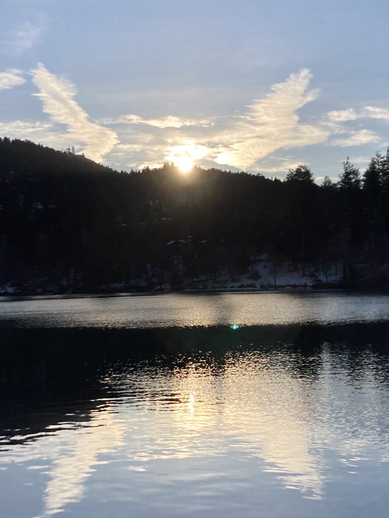 Sunset over a lake with a forest in the background and clouds in the sky in the shape of angel wings.  