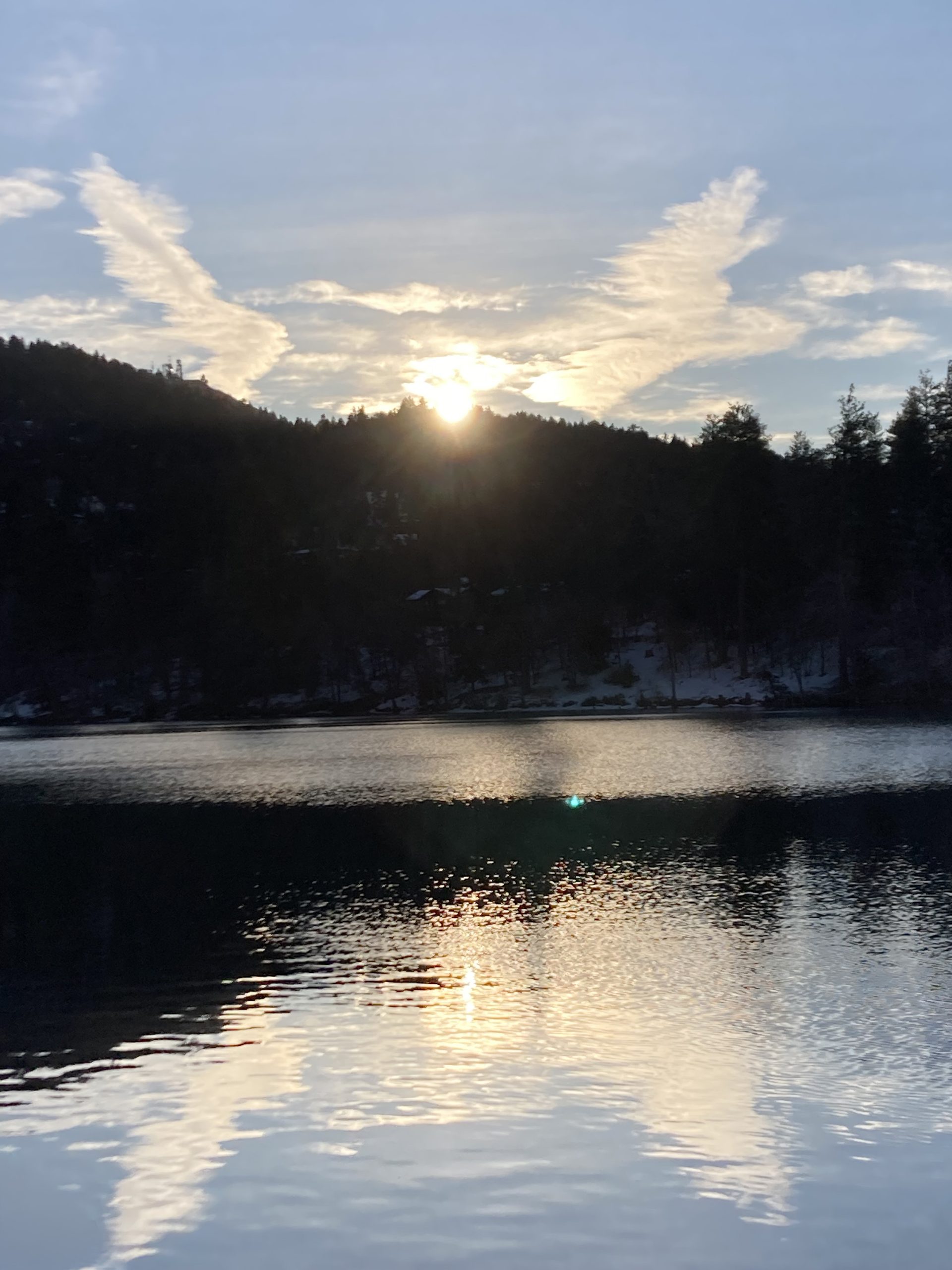 Sunset over a lake with a forest in the background and clouds in the sky in the shape of angel wings.