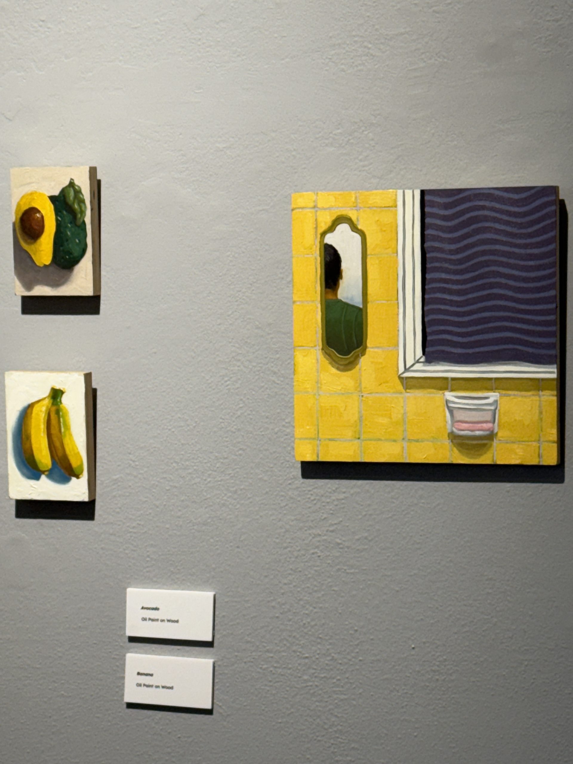 Artwork display featuring three paintings on a gray wall.