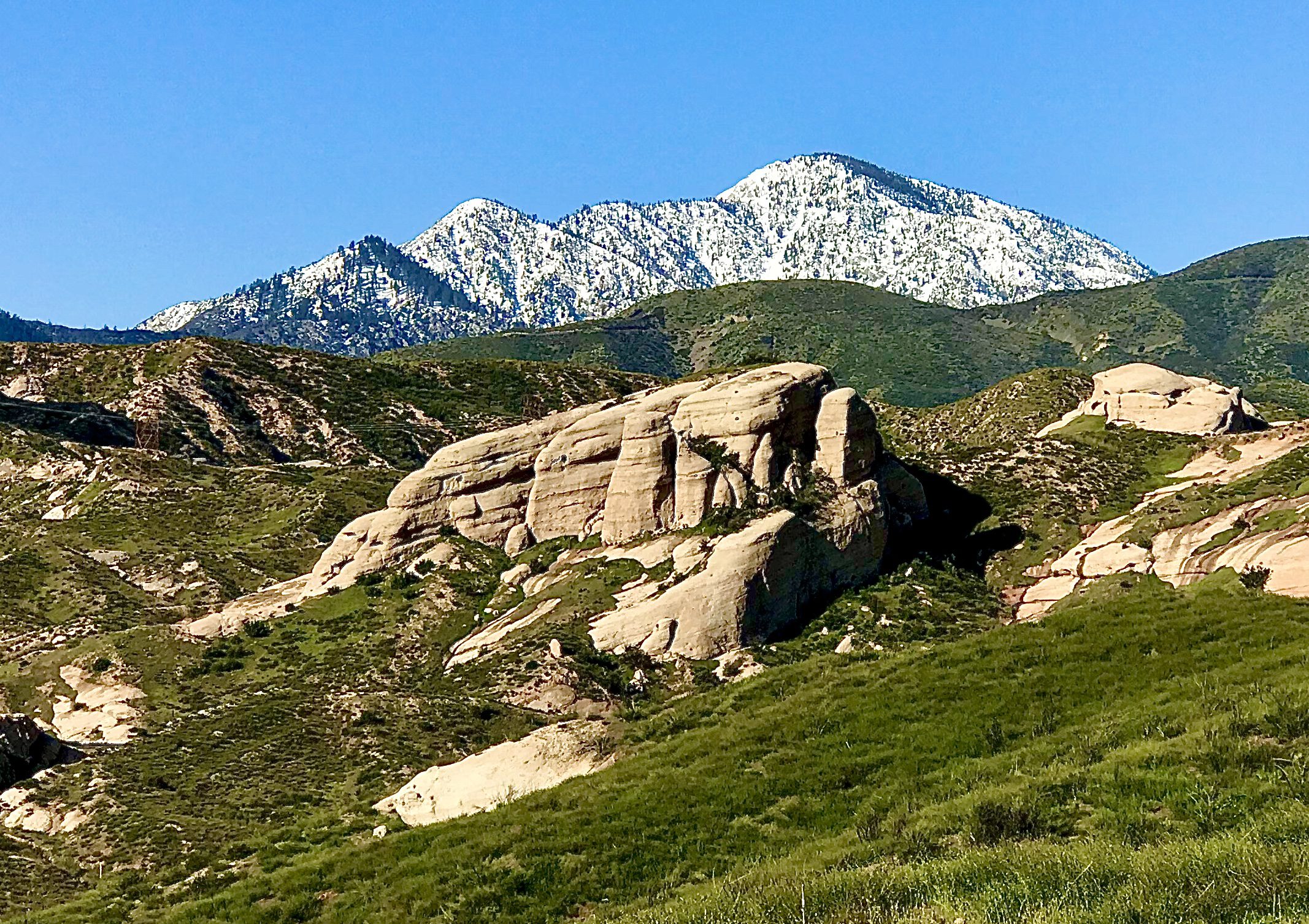 Rock formations with green hills in the foreground and snowy mountains in the background.