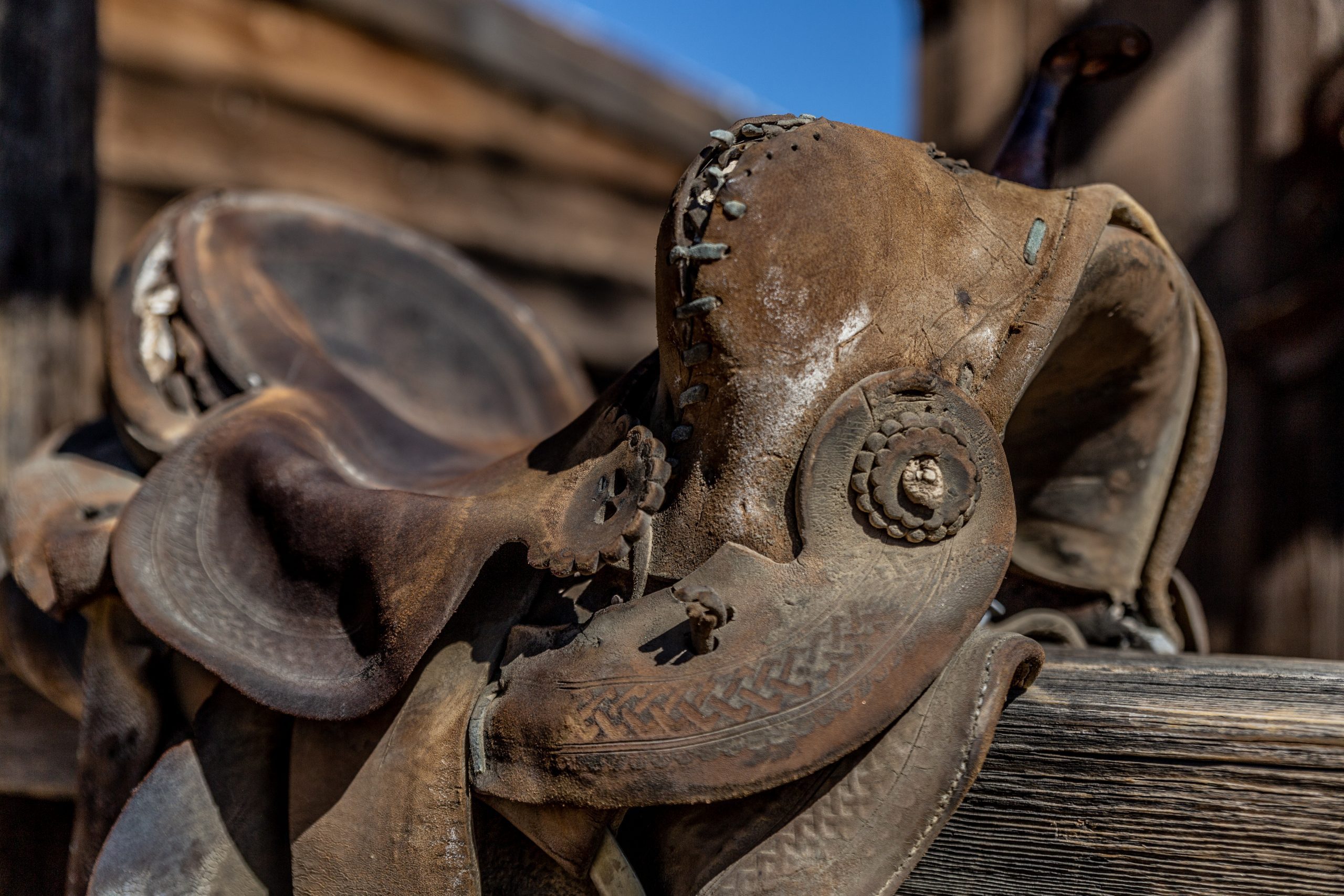 A leather horse saddle is draped over a wooden fence.
