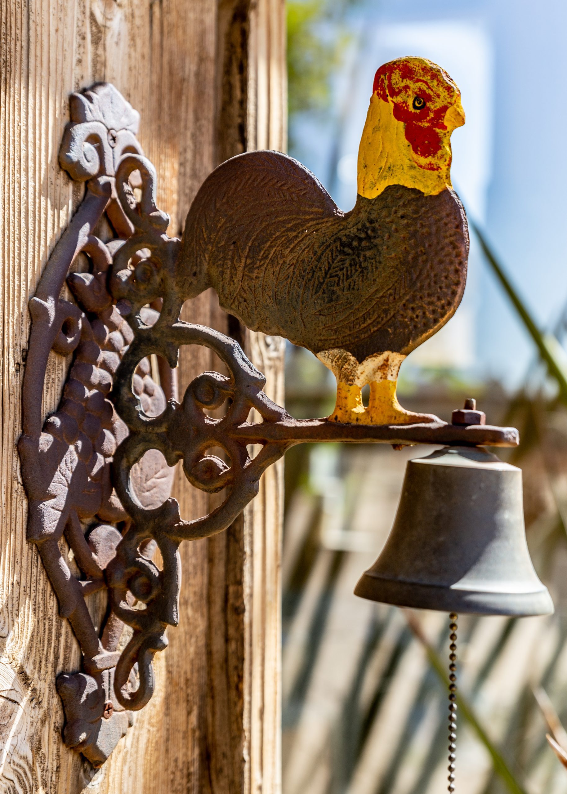 A metal bell mounted on a wooden surface with a decorative rooster design on top.