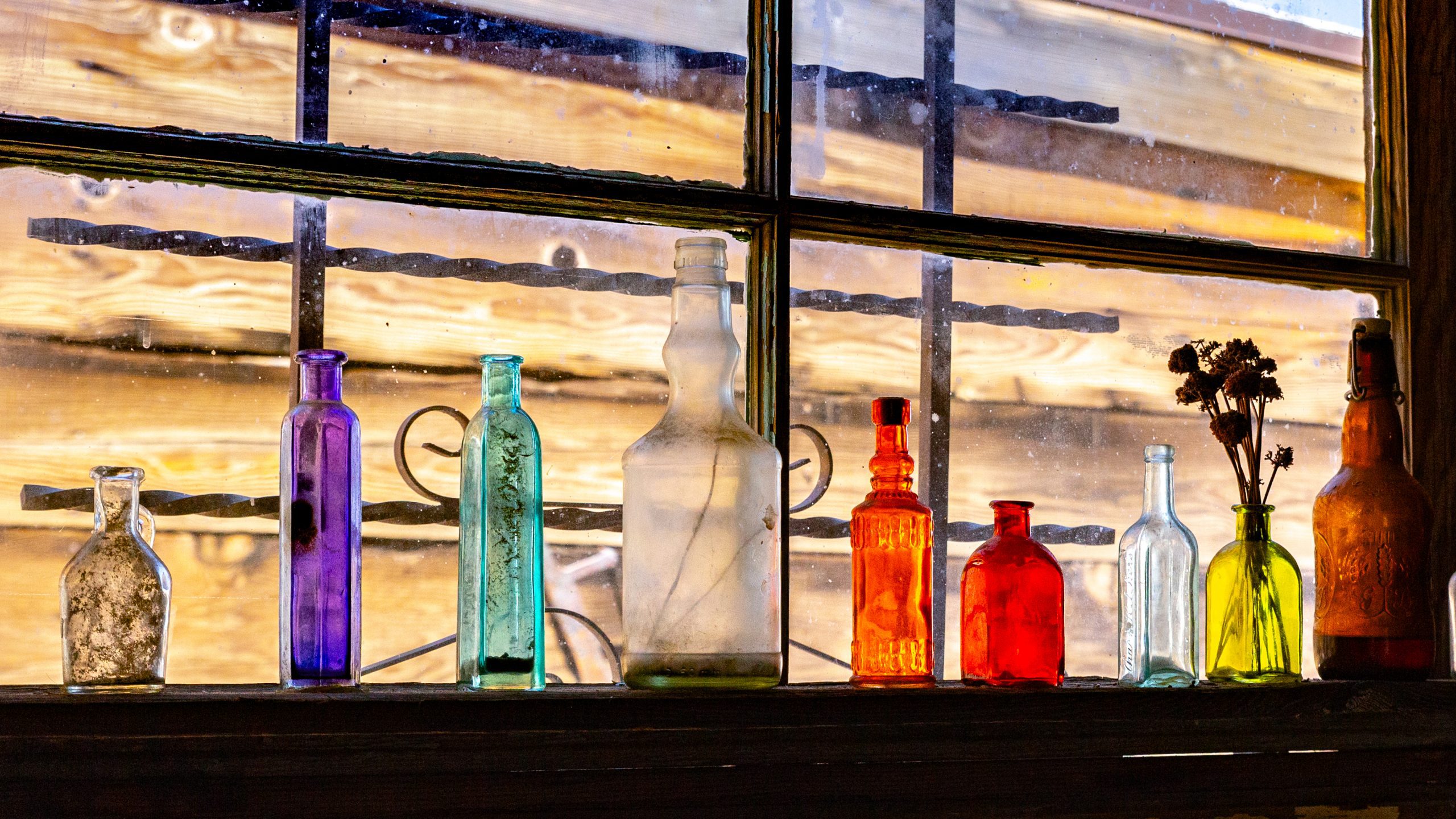 Colorful glass bottles are displayed on a windowsill.