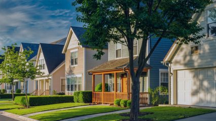 Suburban homes with neat lawns, varied siding, and gabled roofs beneath a partly cloudy sky.
