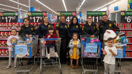 Probation officers and children smile inside a store during Shop With a Cop, standing behind decorated carts filled with toys and gifts.