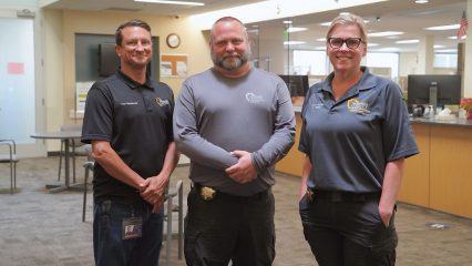Two men and a woman stand together inside an office workspace.