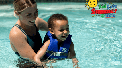 Smiling woman helps a young boy in a blue life vest float in a swimming pool, promoting summer water safety with the “Kid Safe Summer” campaign logo.