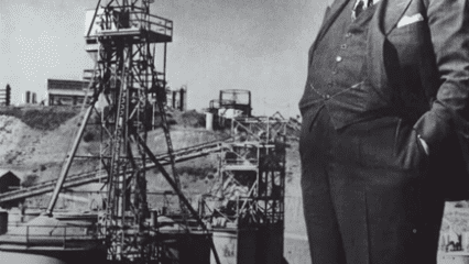 Photo of Henry J. Kaiser standing in front of steel mill equipment.
