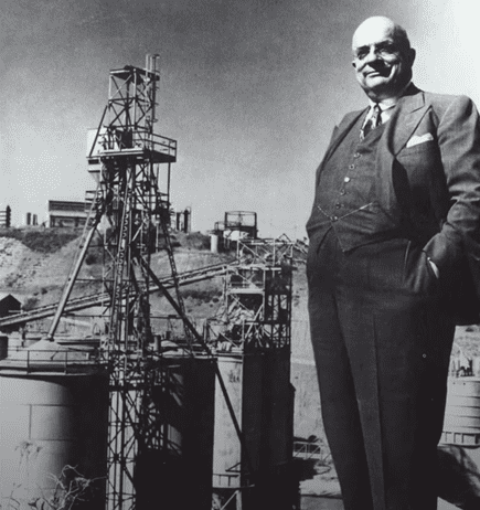 Photo of Henry J. Kaiser standing in front of steel mill equipment.