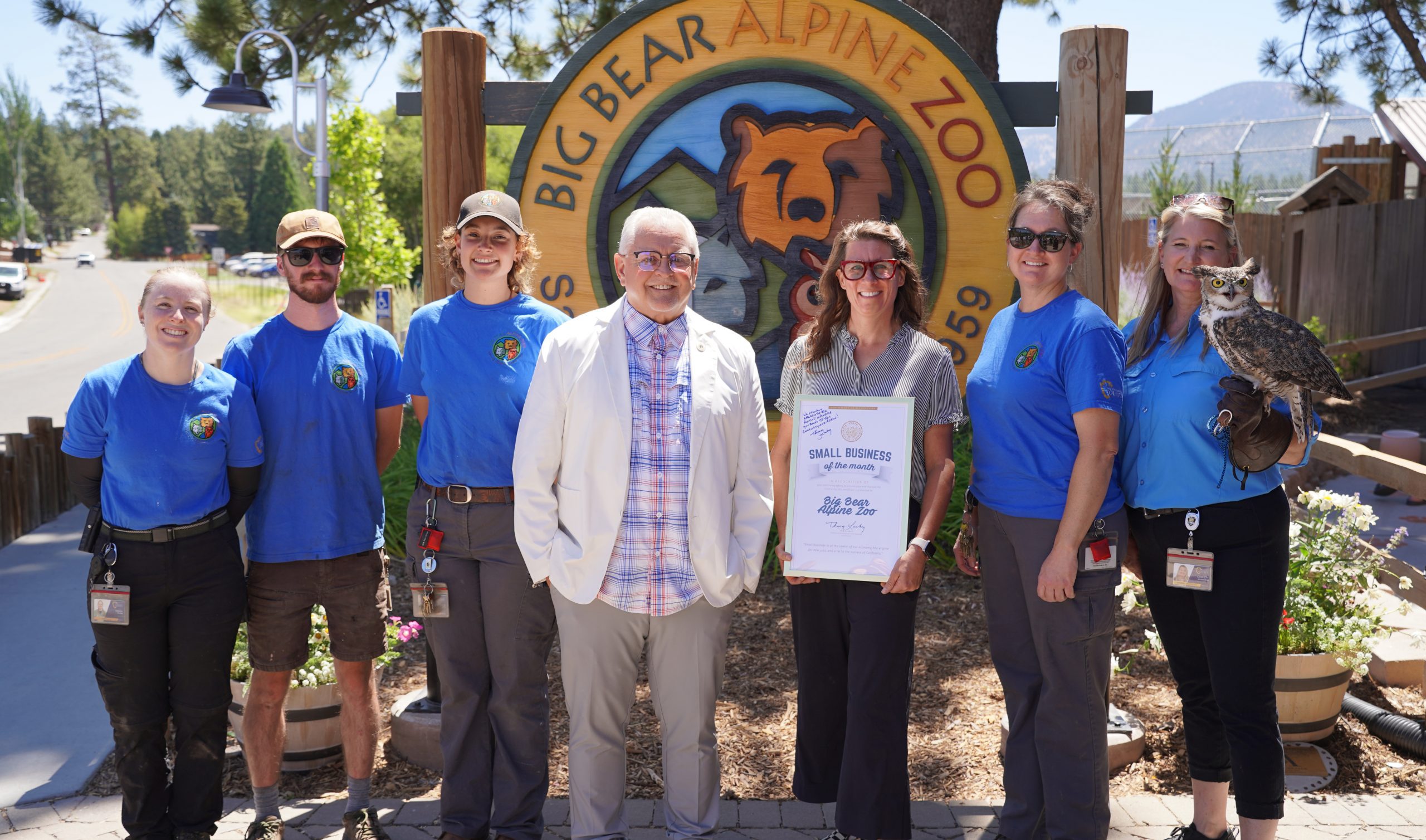 Group of people and an owl in front of the Big Bear Alpine Zoo sign, celebrating a small business award.