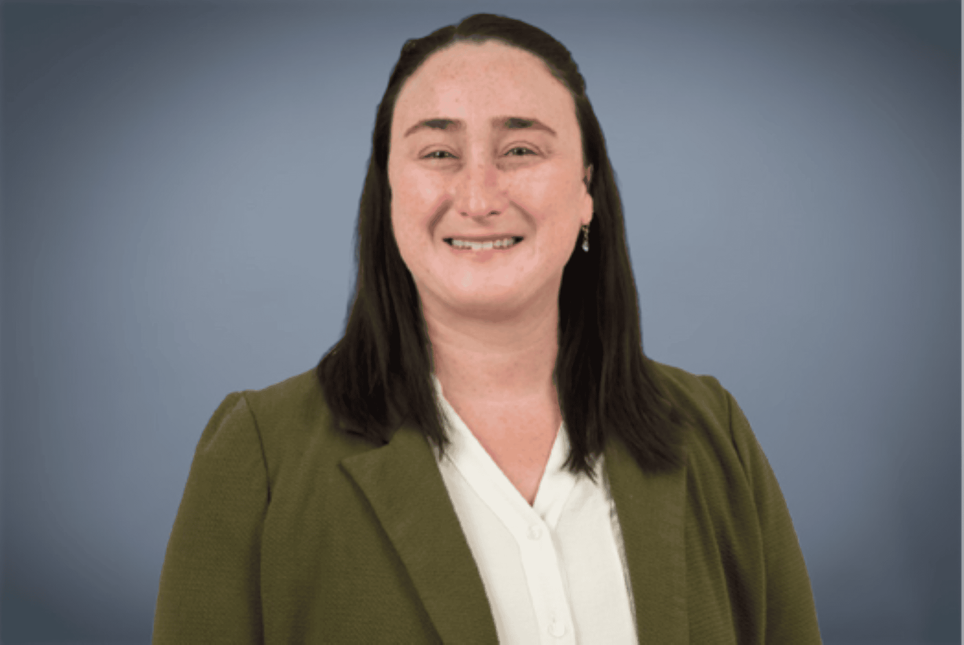 A headshot of a smiling woman wearing an olive blazer and white blouse against a soft gray background.
