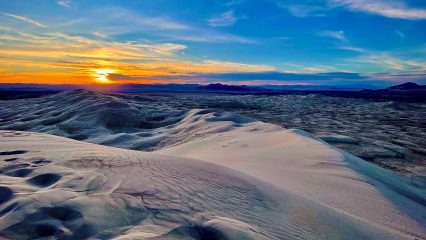 Sunset over sand dunes with a vibrant blue, yellow and orange sky.