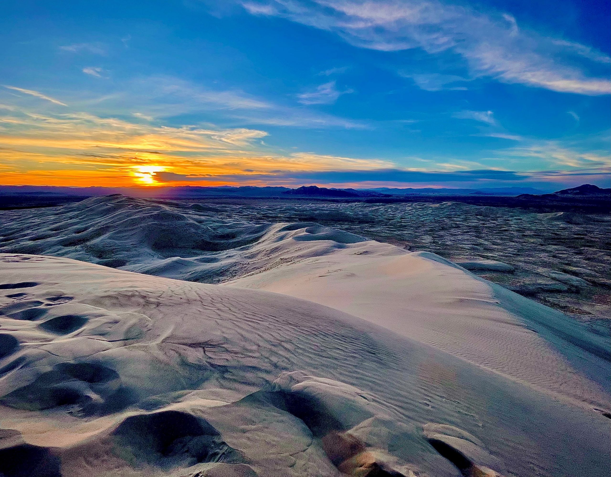 Sunset over sand dunes with a vibrant blue, yellow and orange sky.