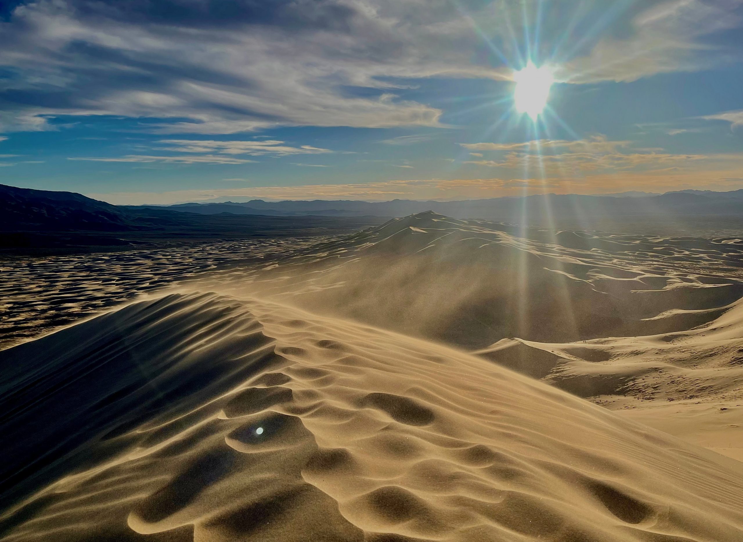 Sun setting over sand dunes with textured sand patterns.