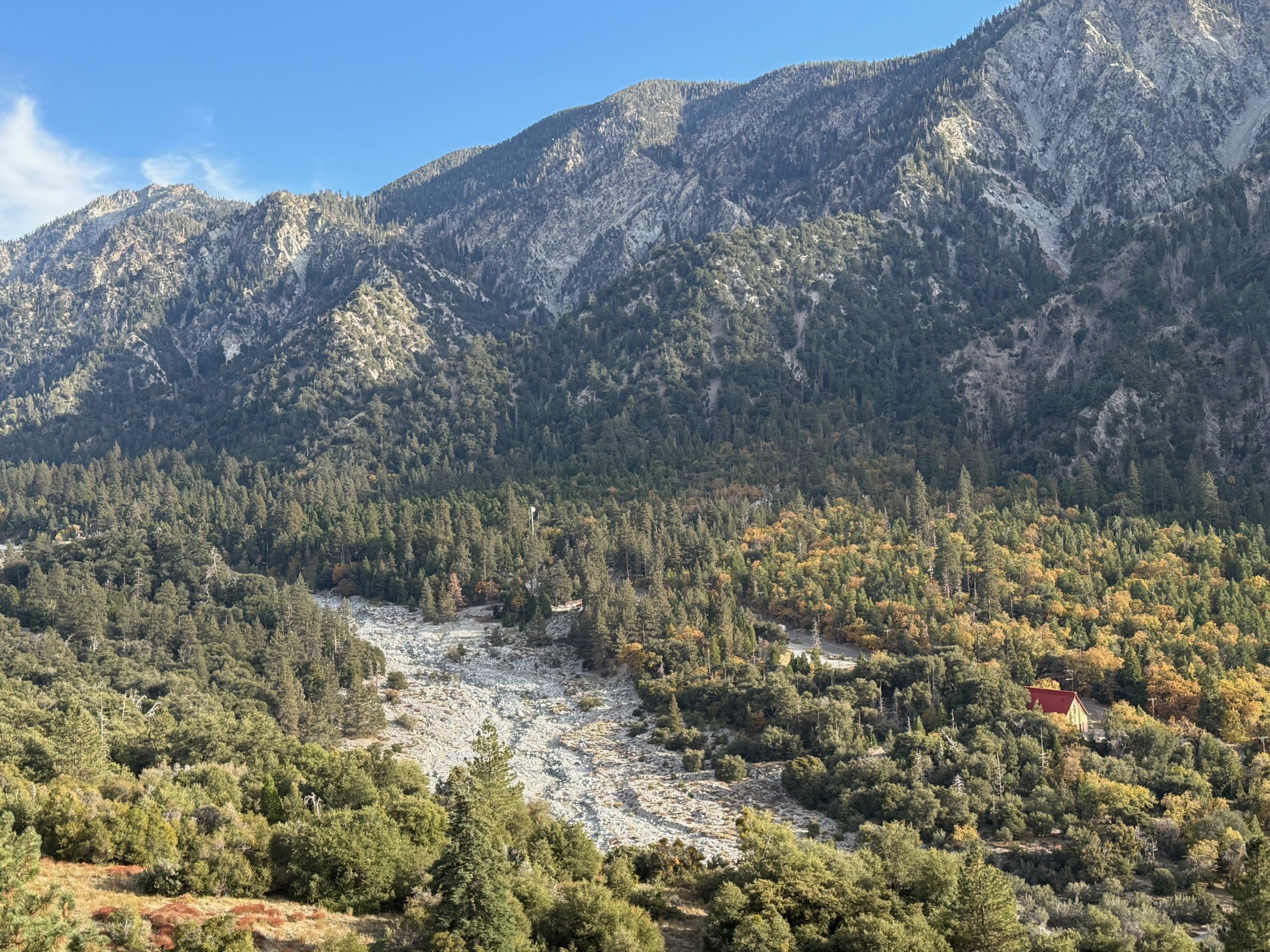View of a dry riverbed winding through a forest. A small building is visible among the trees