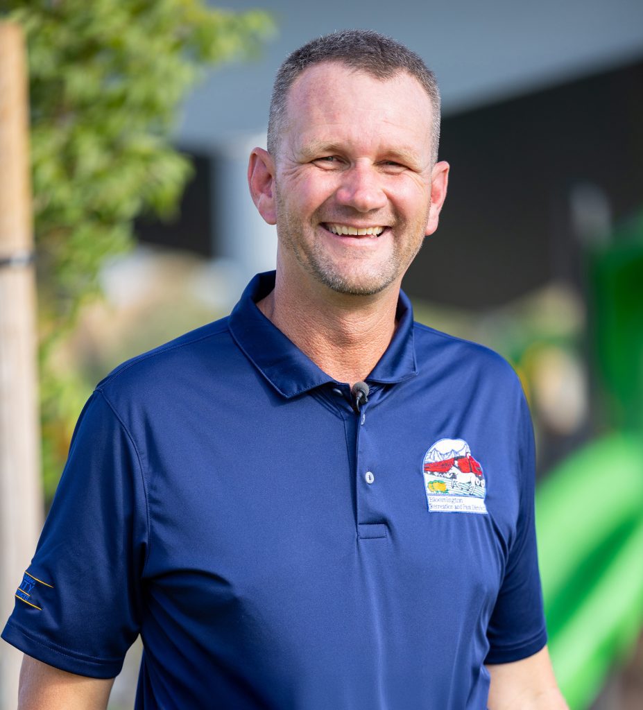 Aaron Speer smiling outdoors in a navy polo with the Public Works Special Districts logo.