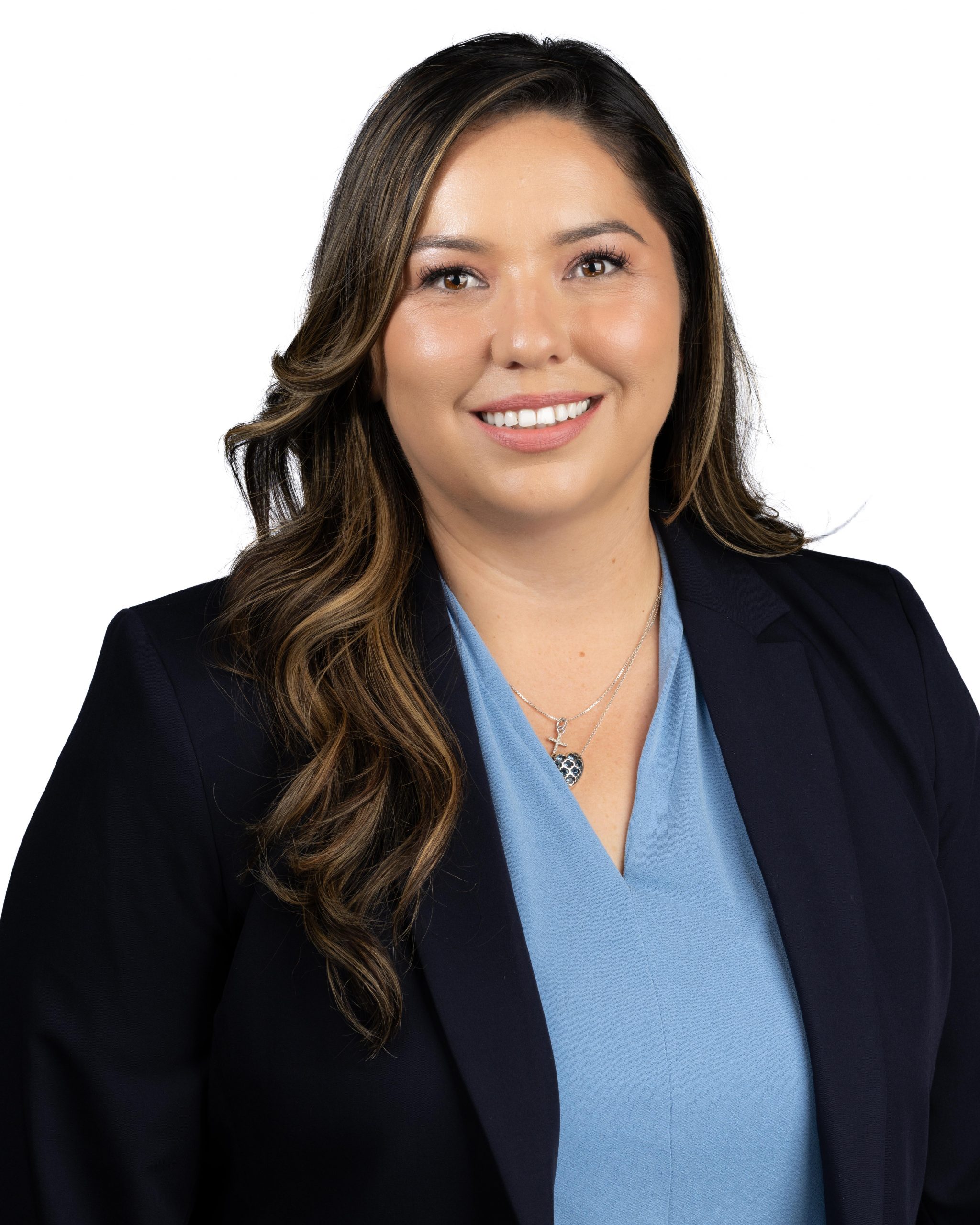 Woman with long wavy hair smiling, wearing a navy blazer and light blue blouse, posed against a white background.