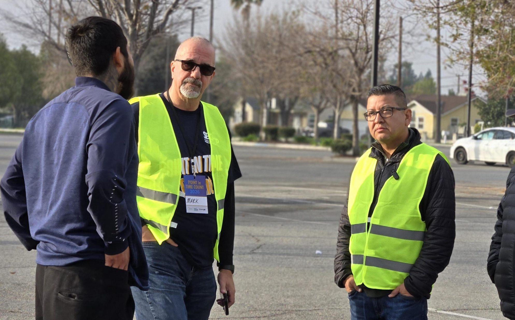 Three individuals engage in a conversation with a homeless person in a parking lot.