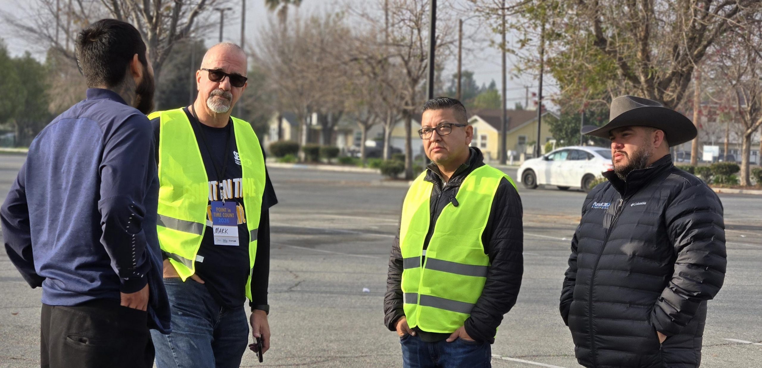 Three individuals engage in a conversation with a homeless person in a parking lot.