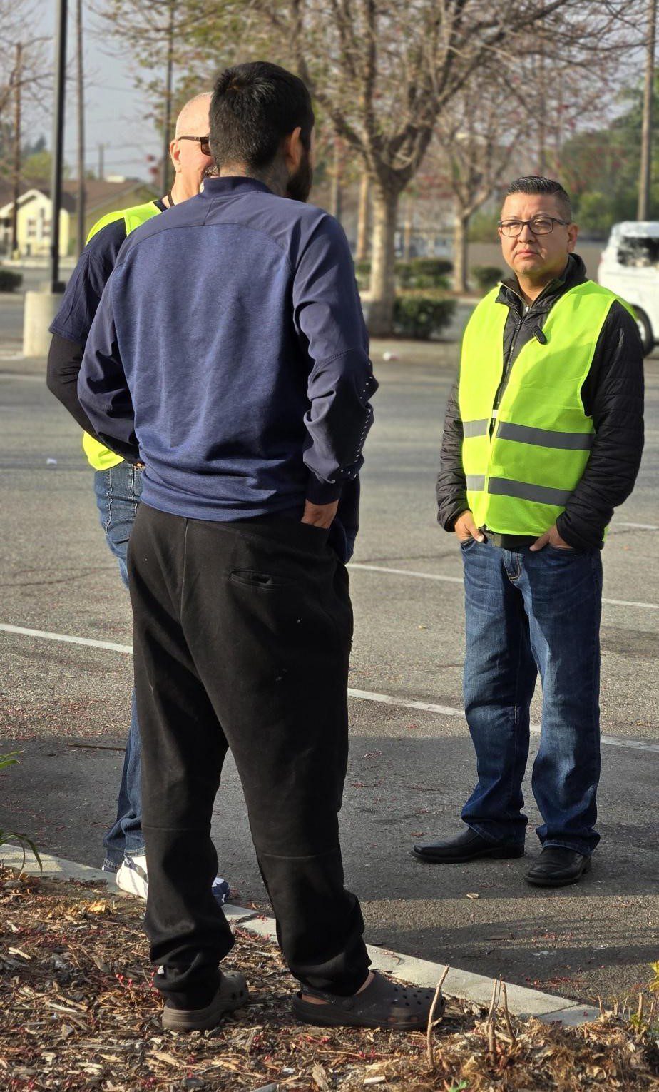 Two individuals engage in a conversation with a homeless person in a parking lot.