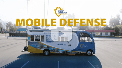 The Public Defender’s Office’s Mobile Defense Program bus with a video play button overlay, indicating a video.