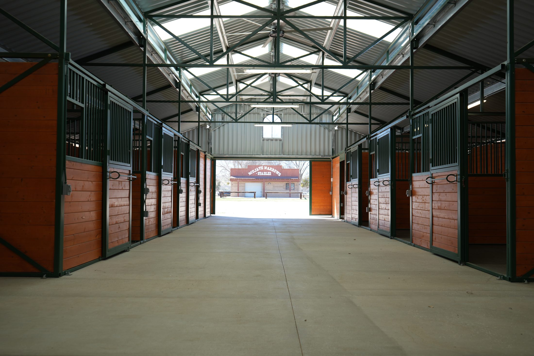 The inside view of the new barn and stalls with a glimpse of an older stable building visible through the open barn doors.