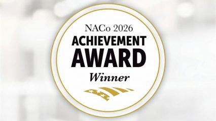 Circular gold-and-white seal with the text “NACo 2026 Achievement Award Winner” against a soft blurred background.