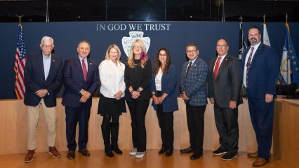 Eight people standing side-by-side in front of a meeting dais.