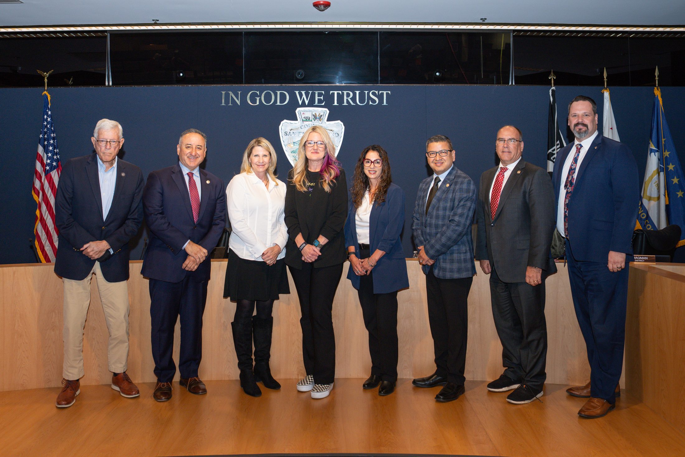 Eight people standing side-by-side in front of a meeting dais.