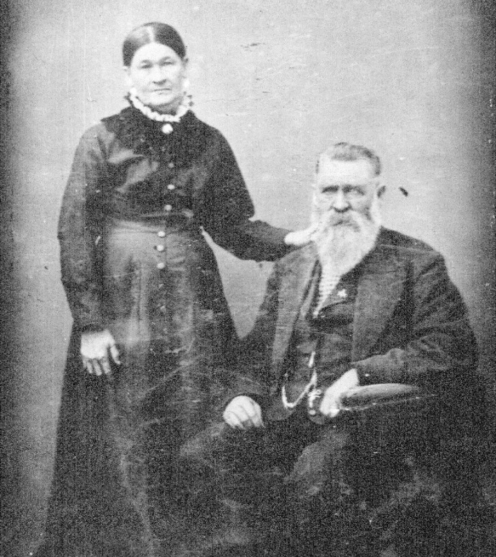 Black and white photo of Virgina Earp standing beside Nick Earp as he’s seated in a chair. They’re dressed in 19th century attire.