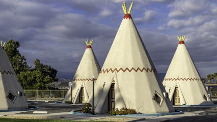 Four cone structures that resemble teepees under a partly cloudy sky.