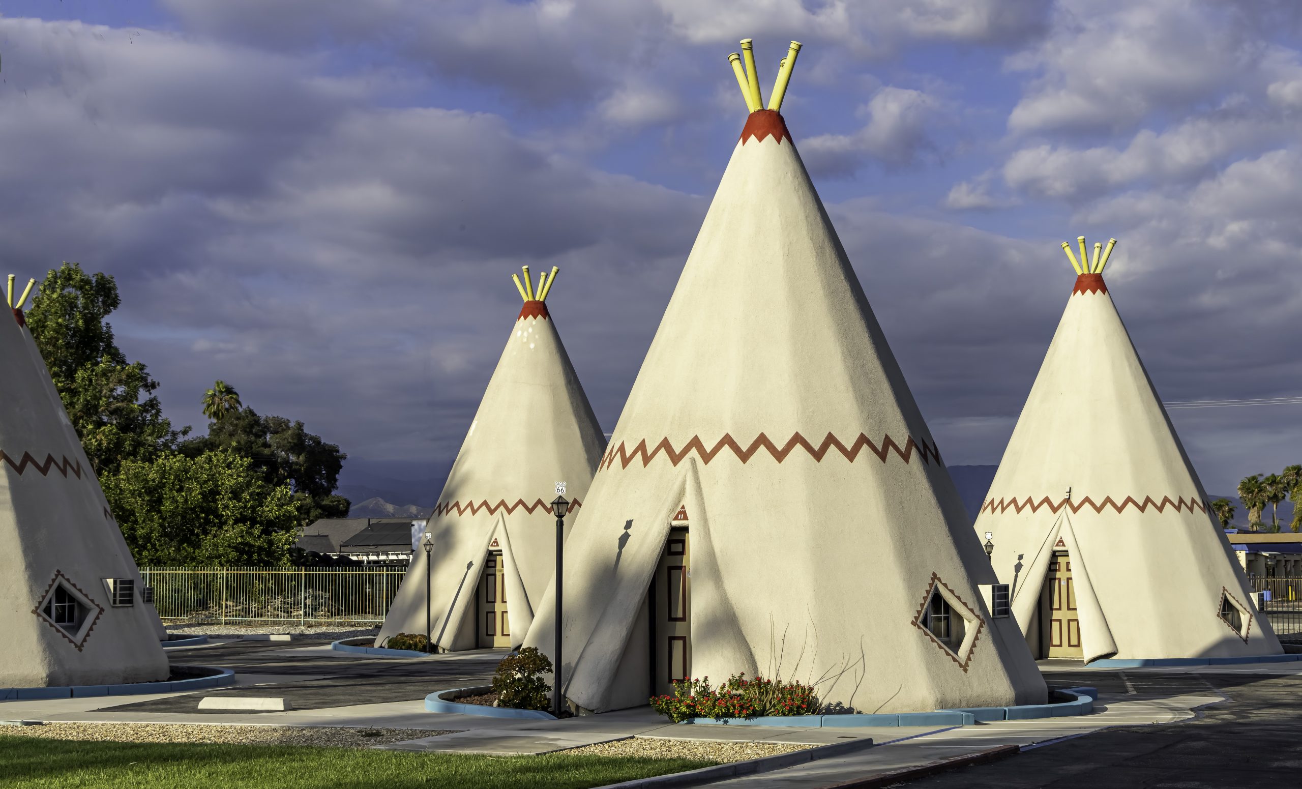 Four cone structures that resemble teepees under a partly cloudy sky.