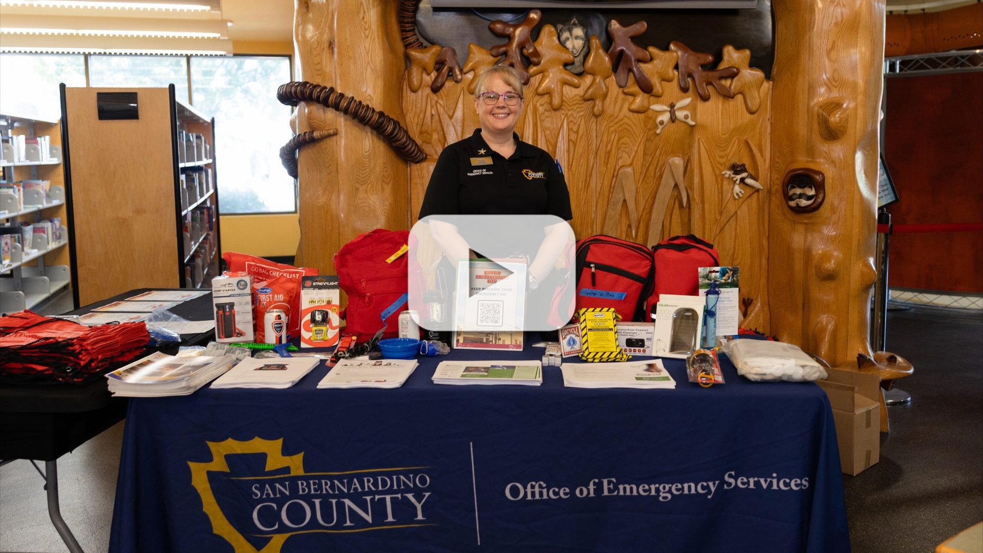 San Bernardino County Office of Emergency Services staff member stands behind a table displaying emer-gency preparedness supplies and information.