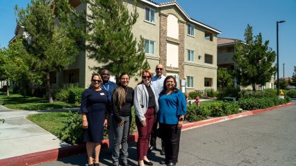 A group of people standing on a street in front of an apartment building.