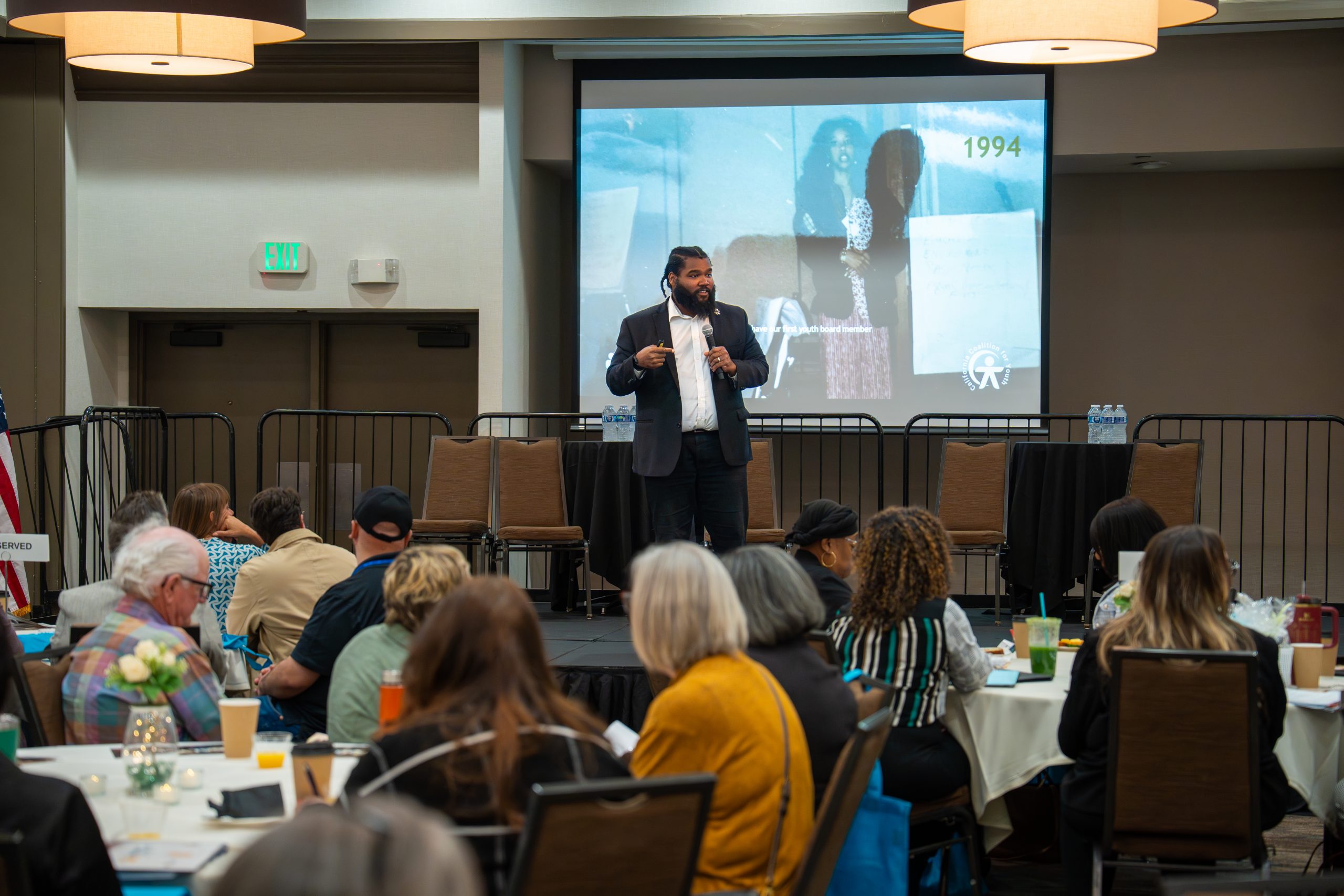 A man on a stage delivering a speech in front of a room full of people.