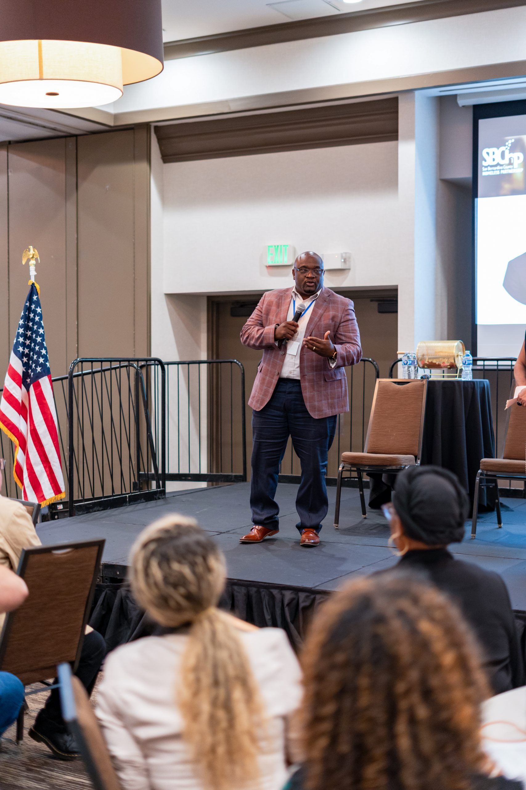A man in a suit with a microphone speaks before a room full of people.