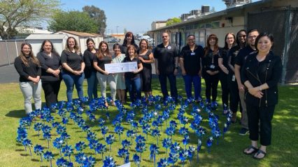 Group of people dressed in dark colors stand in front of a heart-shaped garden made of blue and silver pinwheels.