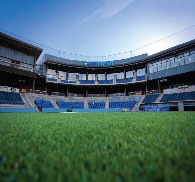 Low-angle view from the grass field inside an empty stadium with rows of blue seats, and the words “ONT FIELD” displayed above the concourse.