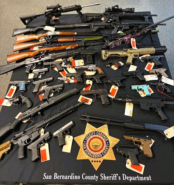 Table with rifles, shotguns, and handguns tagged as evidence; sheriff badge emblem; text: San Bernardino County Sheriff's Department, Sheriff-Coroner San Bernardino County.