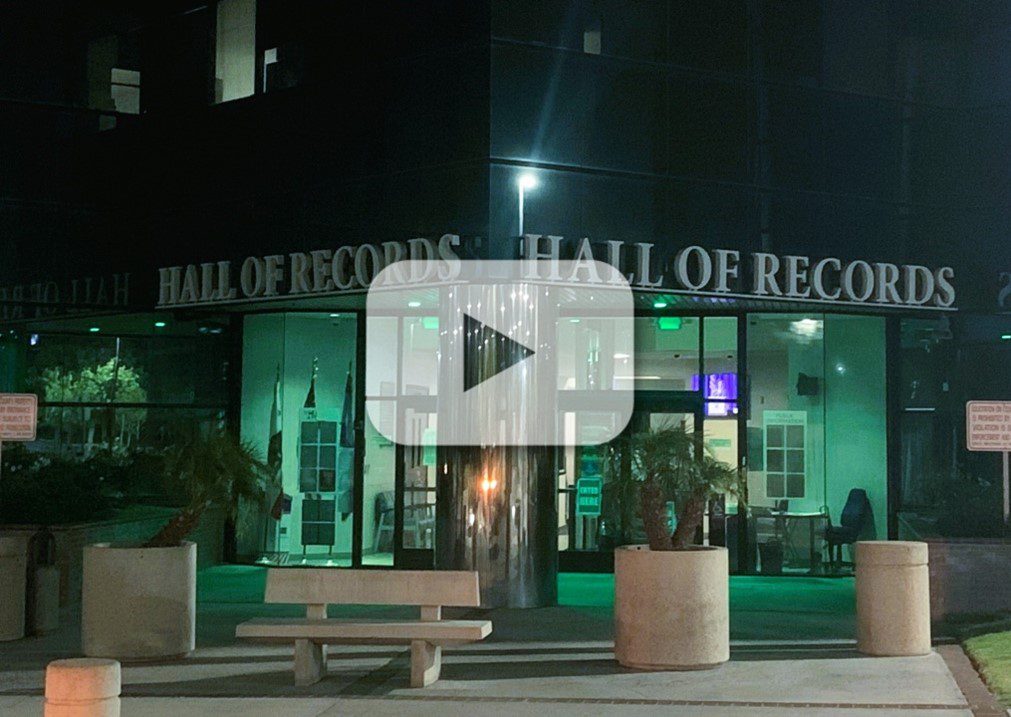 San Bernardino County Hall of Records building lit with green lights at night and a video play button; text on building reads “Hall of Records."