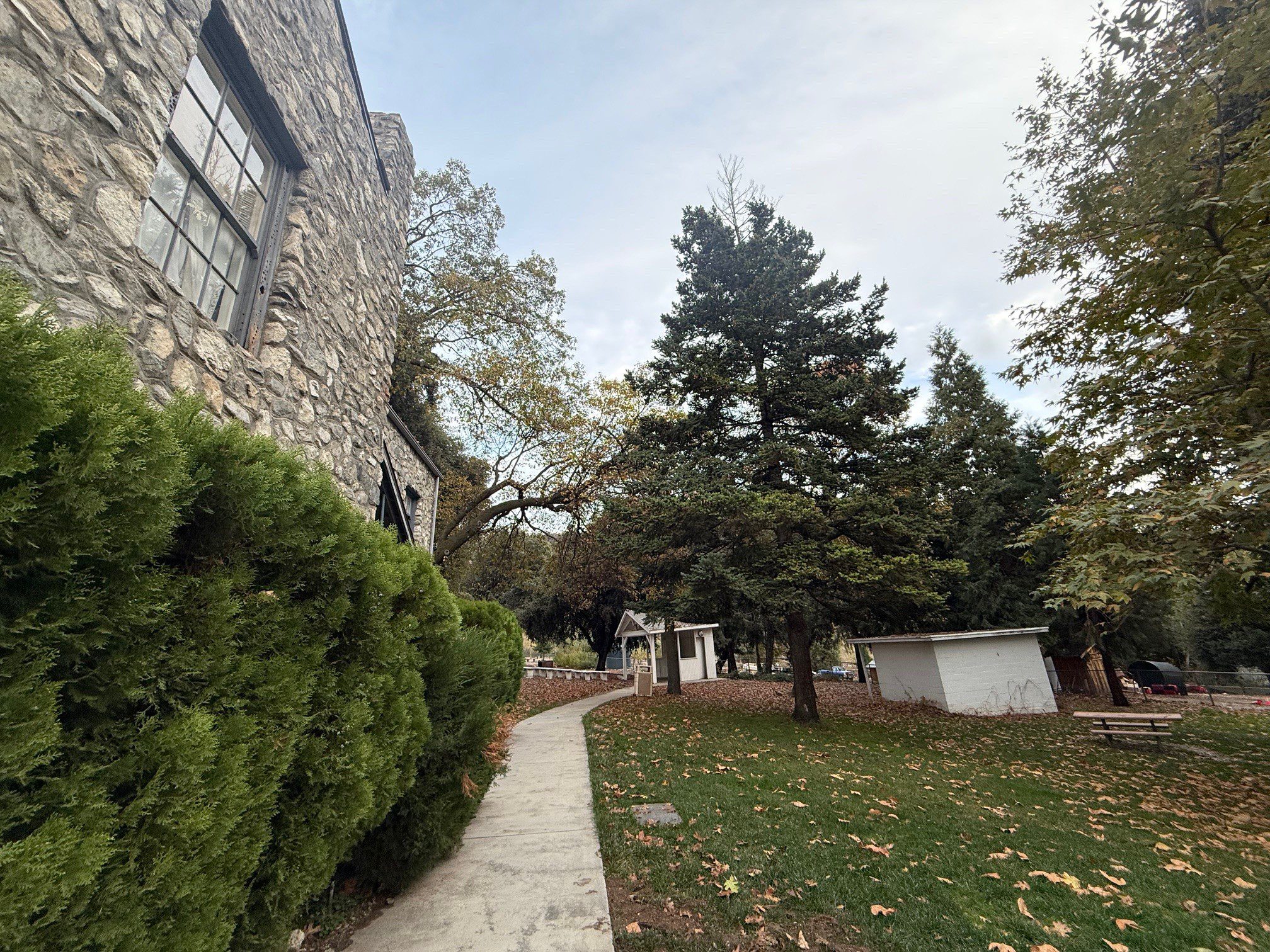 Stone building with a pathway leading past green bushes and trees.