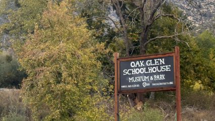 Sign for Oak Glen Schoolhouse Museum & Park in front of trees and a mountainous background.
