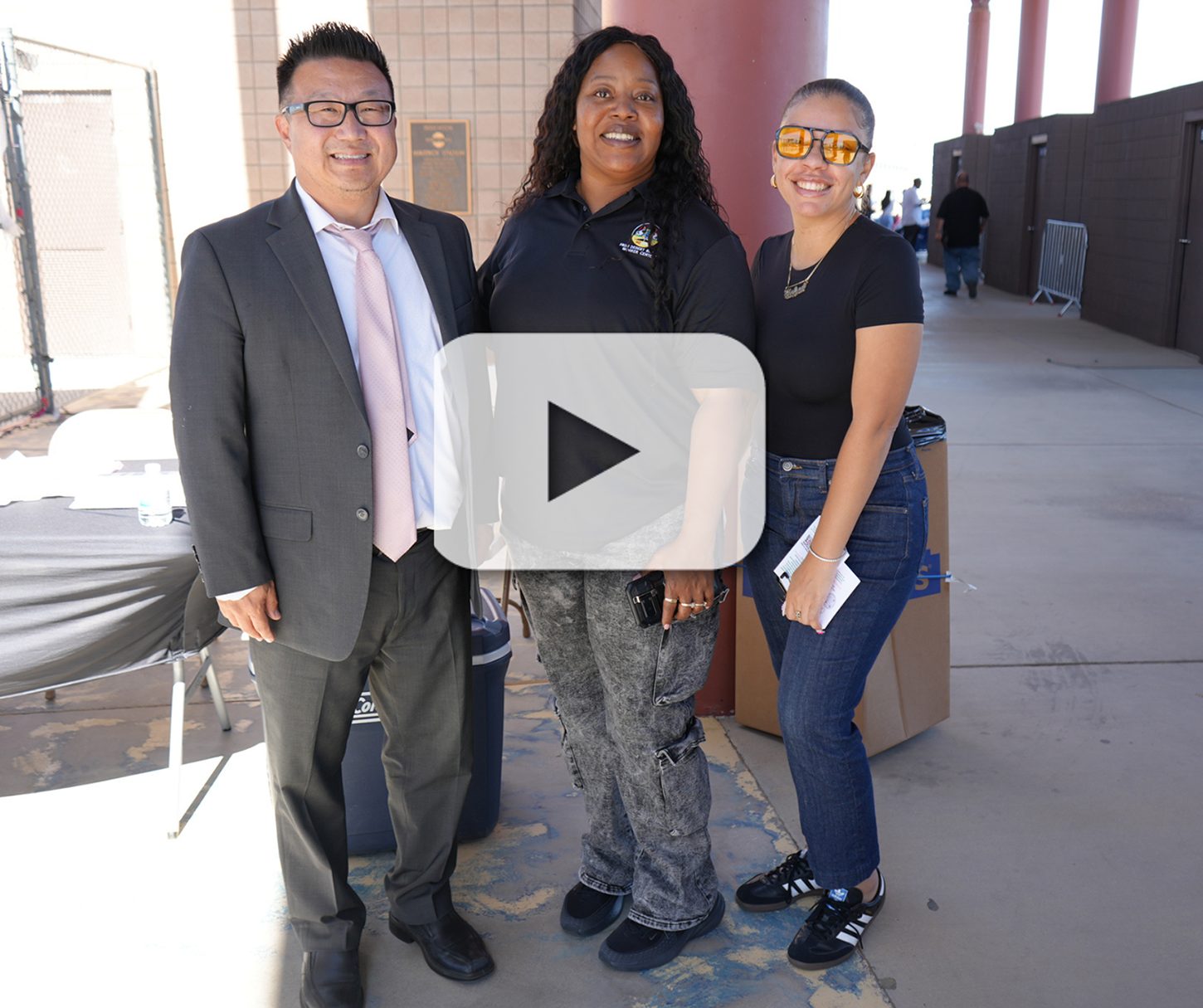 Two women and a man standing outside and smiling at the camera.