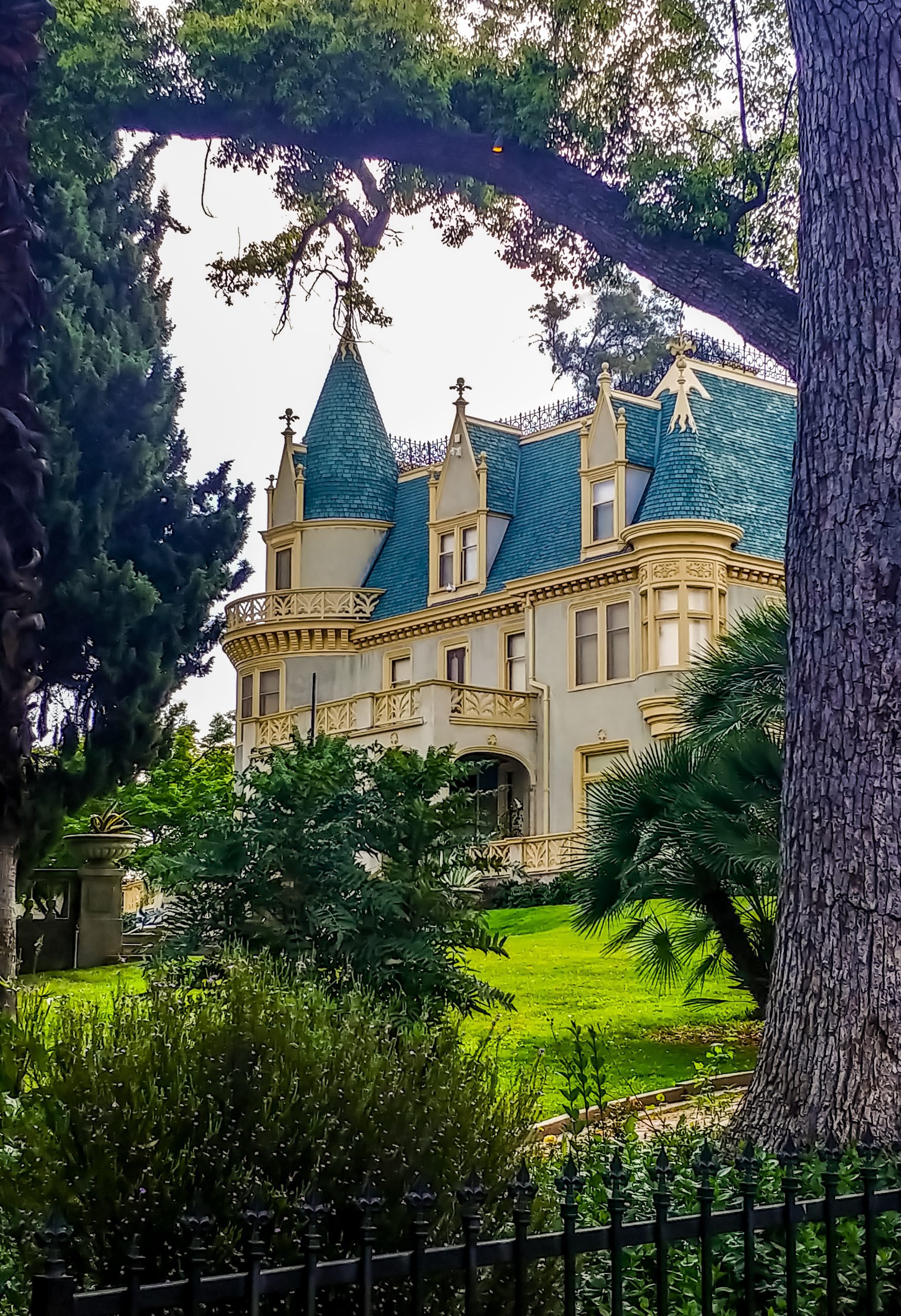 View of the Kimberly Crest House and Gardens, framed by dark trees and a wrought iron fence.