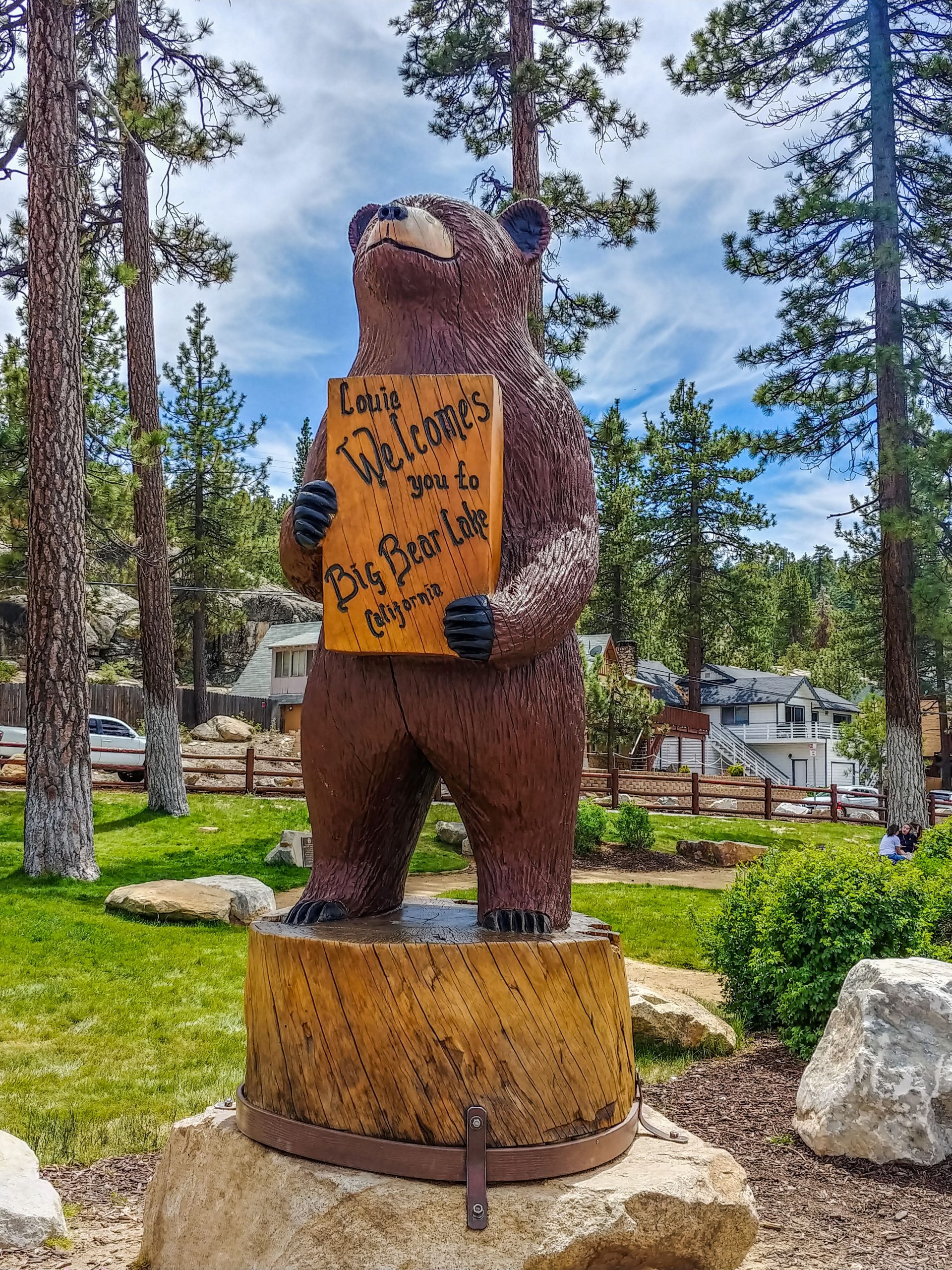 Statue of a bear names Louie with a welcome to Big Bear Lake sign and trees in the background.