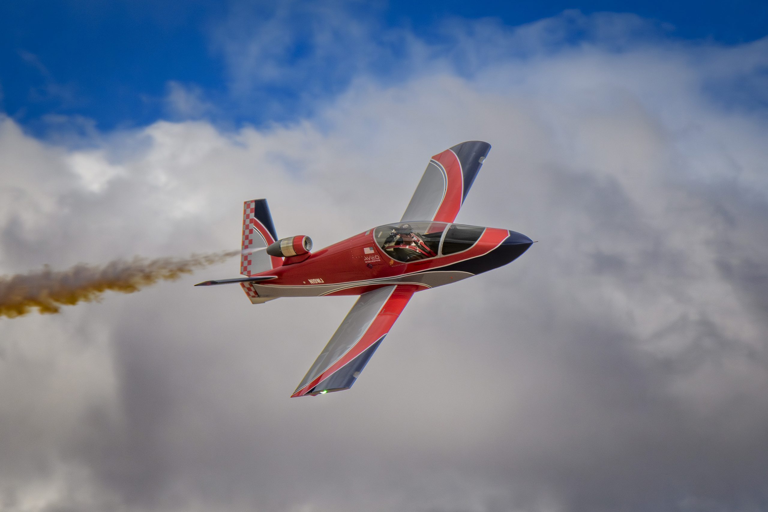 A small red and dark blue plane is flying across the sky and leaving a trail of smoke.