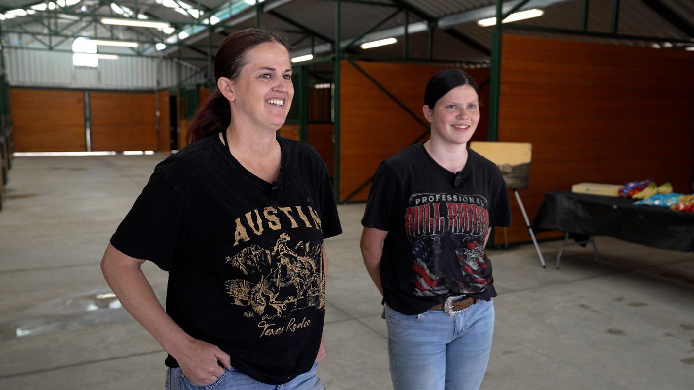 A mother and daughter stand and smile inside a barn.