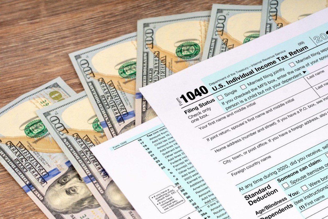 An image of dollar bills and U.S. Individual Income Tax Return 1040 forms lying on a wooden table.