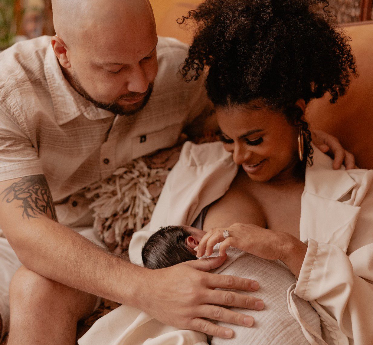 Parent breastfeeds a newborn while another parent sits close beside them.